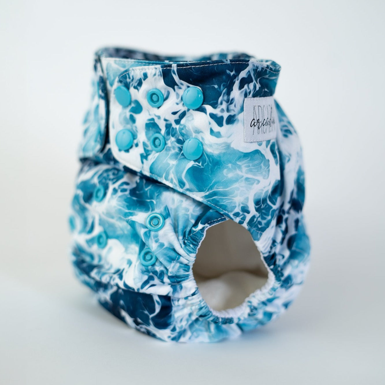 A photo of a cloth diaper in the print Sea Foam, which is a captivating high contrast water/sea pattern. Front angle view.