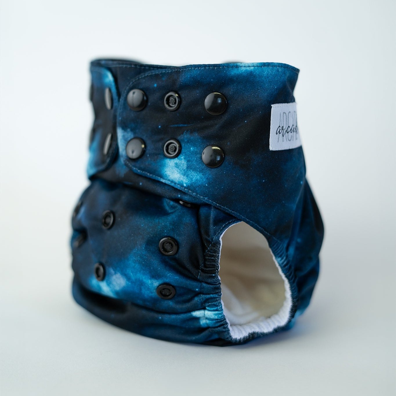 A photo of Cosmos, a cloth diaper with a galactic blue and black print. Deep dark outer space & celestial vibes.