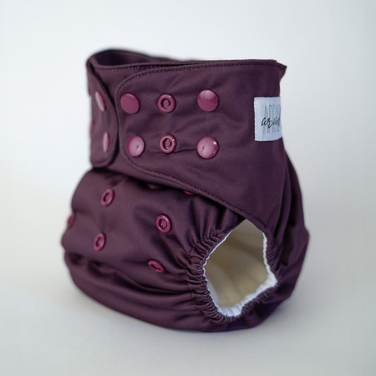 A photo of a wine colored cloth diaper, front angle view. This reusable diaper is called solstice, a burgundy color. Cranberry or garnet, the snaps are also a deep wine color.