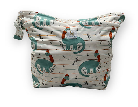 Patterned 3d bottom wet bag with dinosaur design on a white background. The dinosaur has a scarf and winter hat on. You can see the Wickham Wild logo tag, 2 zipper openings, and a small strap with a snap closure. 