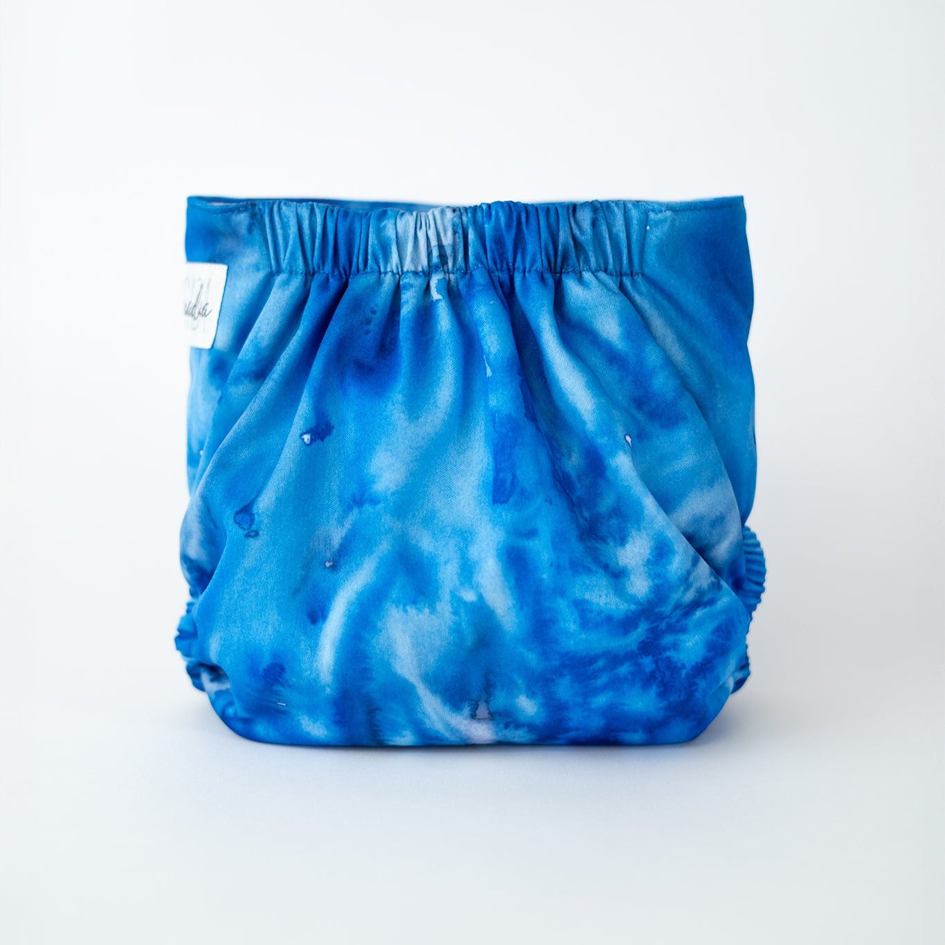 A photo of a vibrant, watercolor blue cloth diaper displayed against a clean, white background. The diaper features an elastic waistband designed to keep your baby comfortable. This modern cloth diaper adds a touch of style with its bold, watercolor-like pattern, making it a perfect choice for parents who value both function and fashion. Rear view.