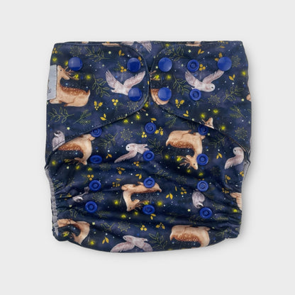 A pocket style cloth diaper with a dark navy background and illustrations of owls, deer, fireflies, and minimalist foliage in yellow. the snaps are dark blue.