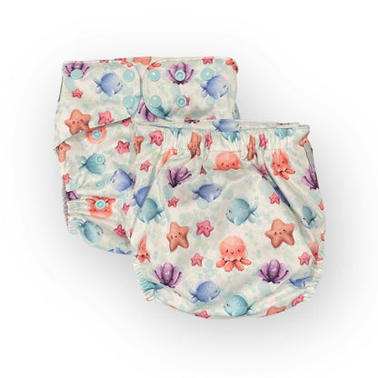a photo showing 2 of the same print pocket cloth diaper. The print background is white with light blue bubbles. The illustrations on the diapers are cute cartoony watercolor ocean critters like sea stars, clams, octopus, and fish.