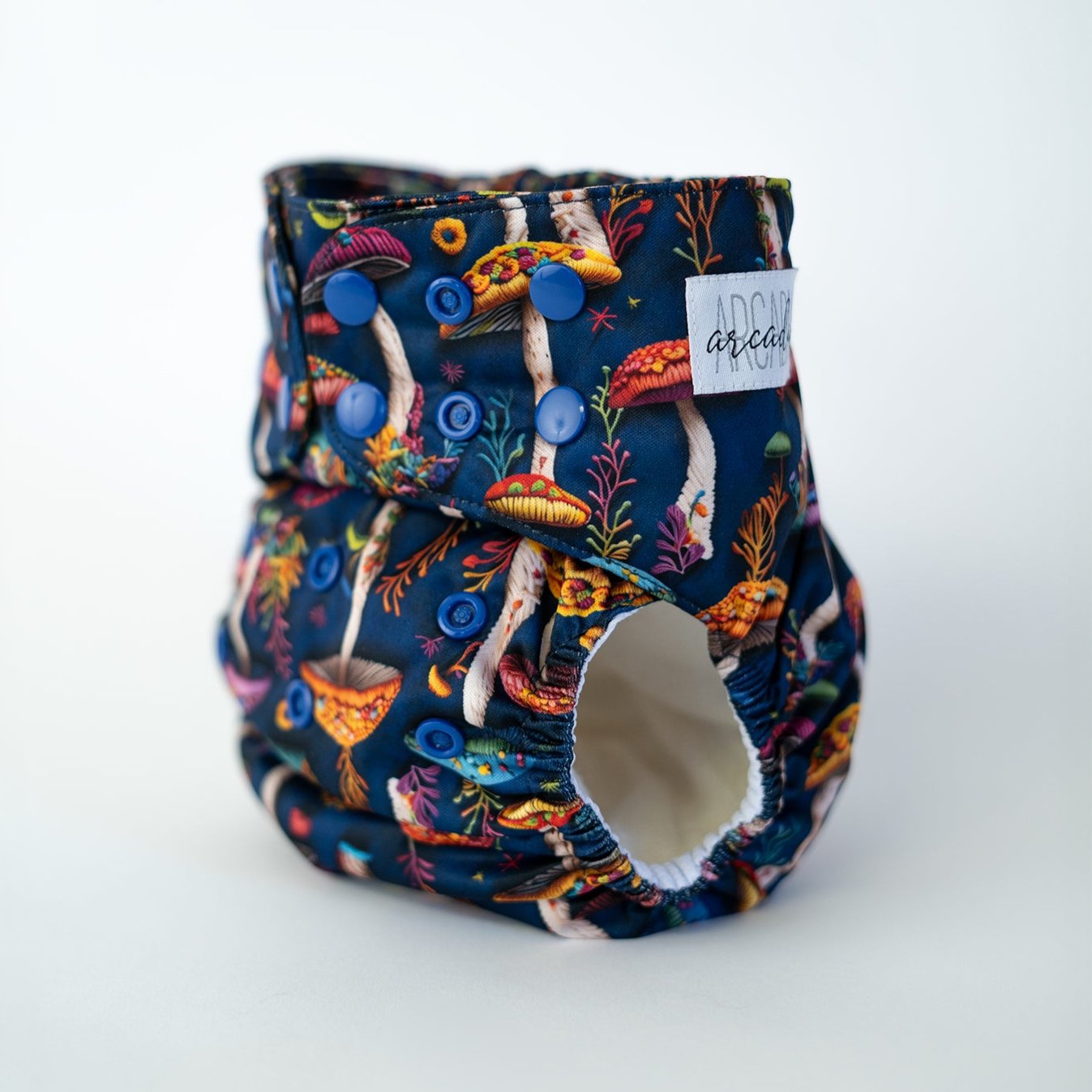 Colorful pocket cloth diaper featuring a vibrant design of faux embroidery mushrooms and foliage against a deep navy blue background. This nature inspired pattern is perfect for parents who want both functionality and a touch of fantasy in their diapering choices. Front angle view.