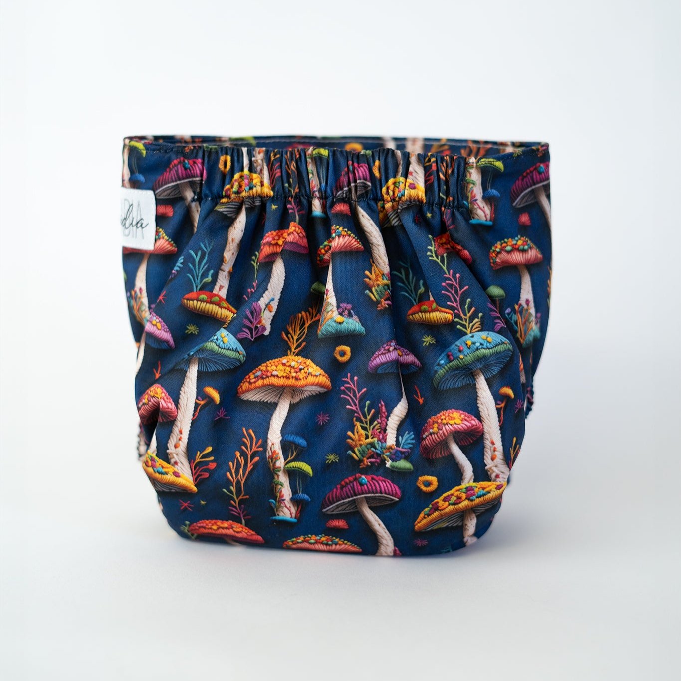 Colorful pocket cloth diaper featuring a vibrant design of faux embroidery mushrooms and foliage against a deep navy blue background. This nature inspired pattern is perfect for parents who want both functionality and a touch of fantasy in their diapering choices. Back view.