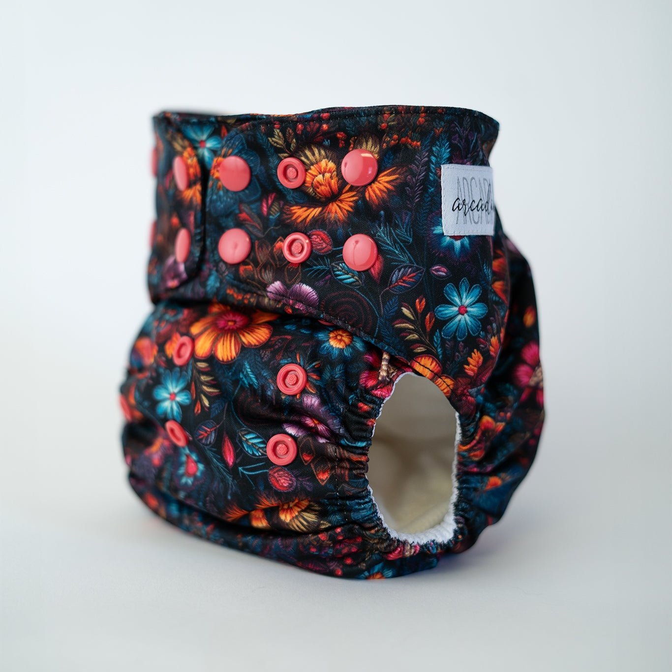 A reusable cloth diaper, the print features a faux embroidery floral design. The colors are bold and rich, with a dark moody background.