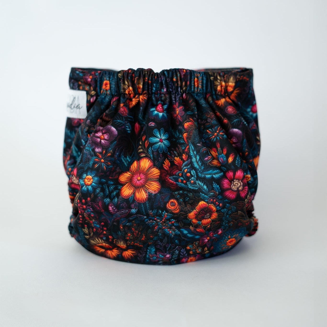 A reusable cloth diaper, the print features a faux embroidery floral design. The colors are bold and rich, with a dark moody background.