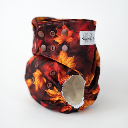 A reusable cloth diaper featuring fall leaves. The autumn leaves are red, orange, and yellow.