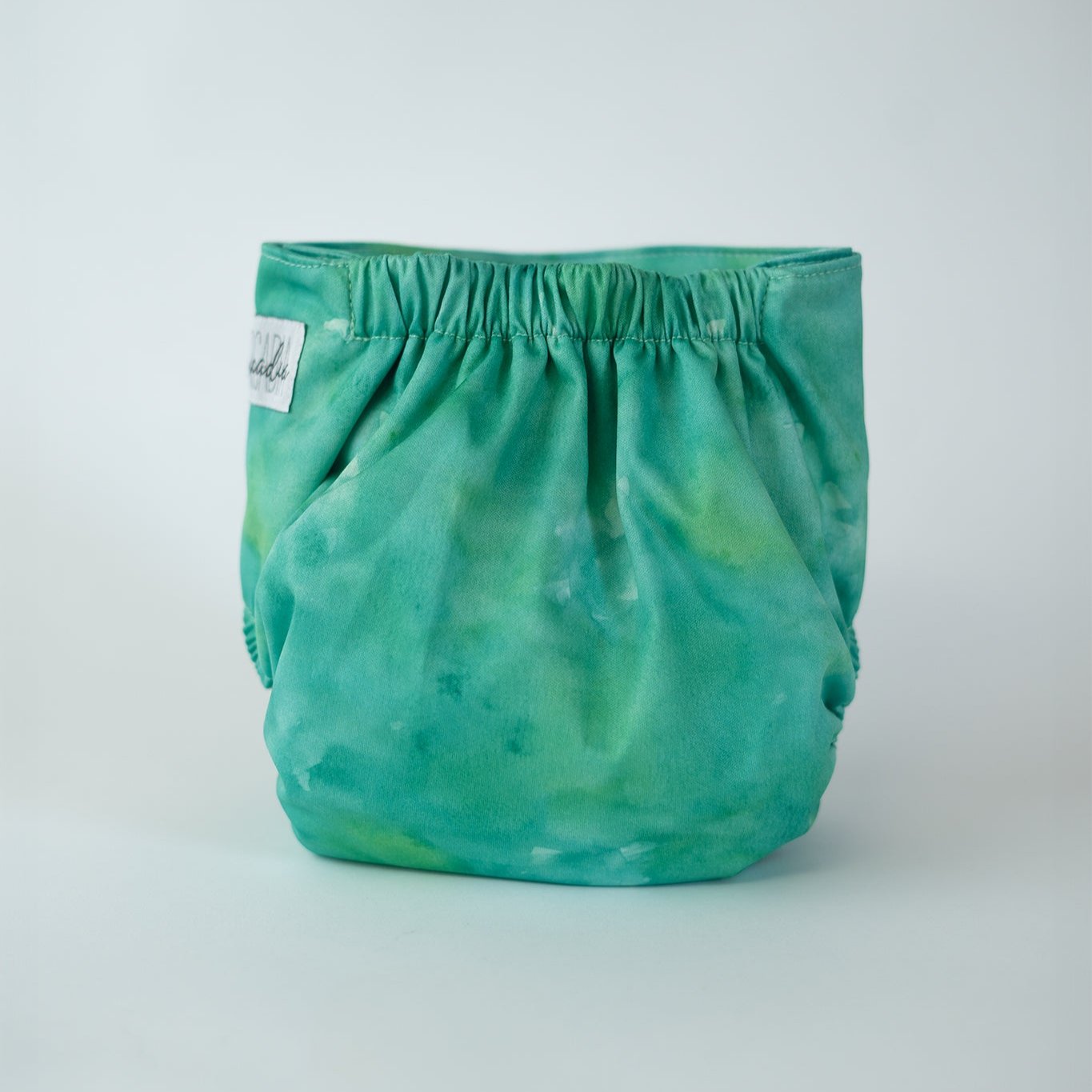 A jade green to emerald cloth diaper with a watercolor design, featuring soft fabric and a snug, elastic waistband for a comfortable fit. Rear view.