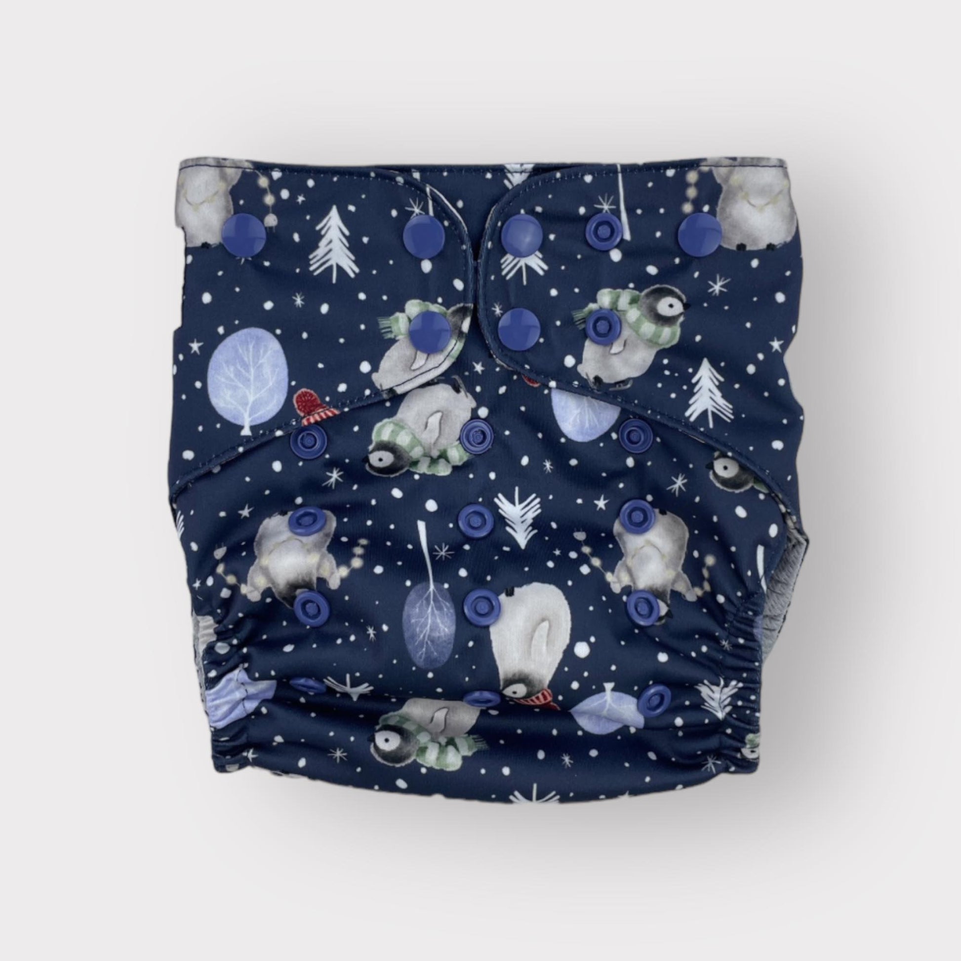 Navy blue background pocket style reusable diaper with penguin illustrations alongside winter trees and snow.