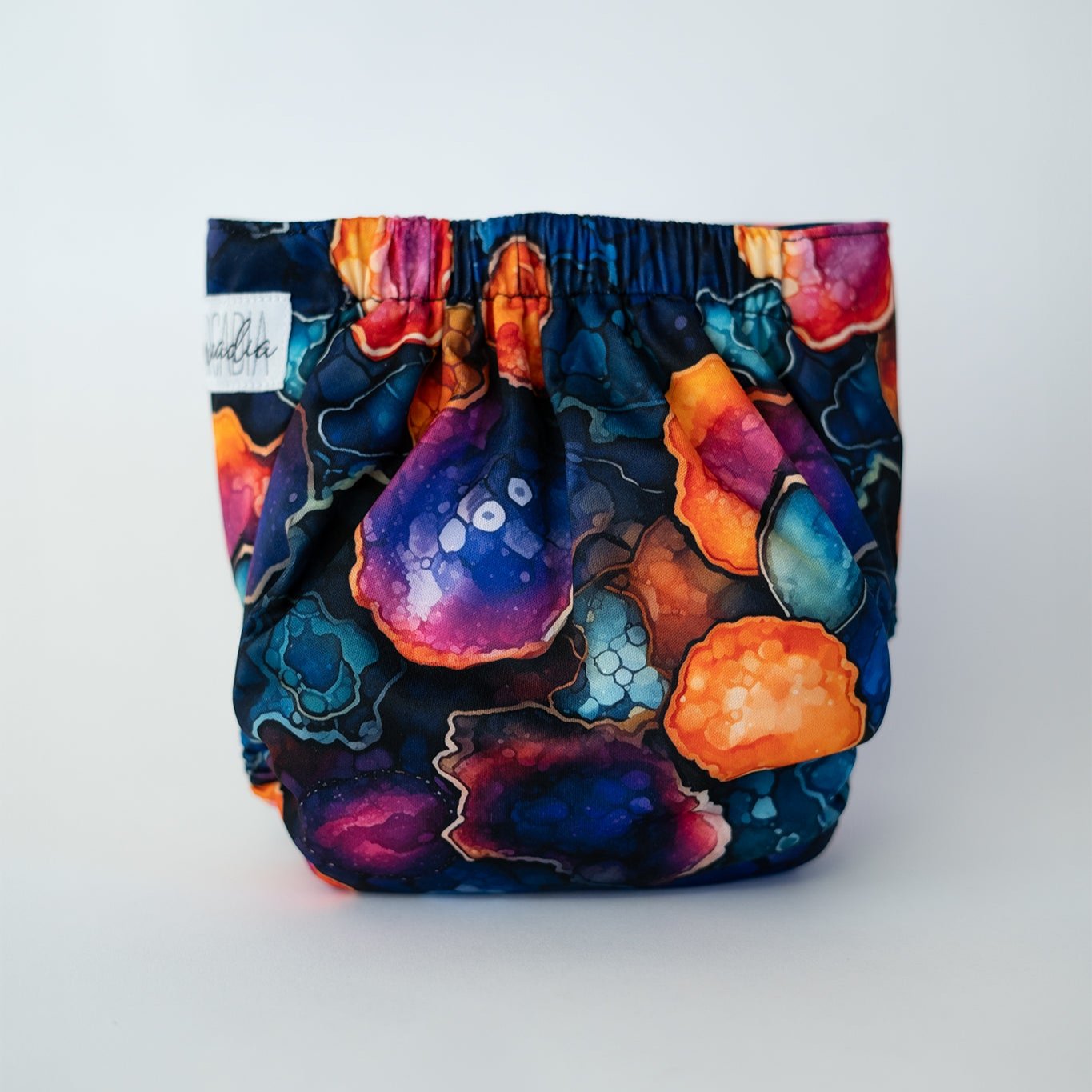 Cloth diaper with a vibrant, gemstone-inspired pattern featuring rich hues of blue, purple, orange, and teal. The unique design showcases intricate crystal like shapes, perfect for parents who love bold and colorful baby accessories. This eye catching diaper offers a stylish and distinctive look for any baby's wardrobe. Rear view.