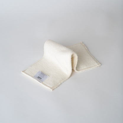 A cream colored cloth diaper insert on a pain white backdrop. the insert is folded in an "inchworm" formation. The insert has squared edges and you can see an information and care tag with the arcadia's nursery logo sewn onto the end.