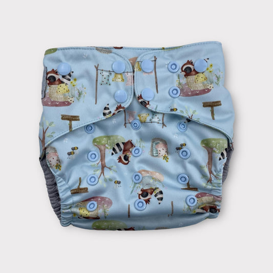 Patterned wickham wild reusable diaper with illustrations of racoons doing laundry on a light blue background
