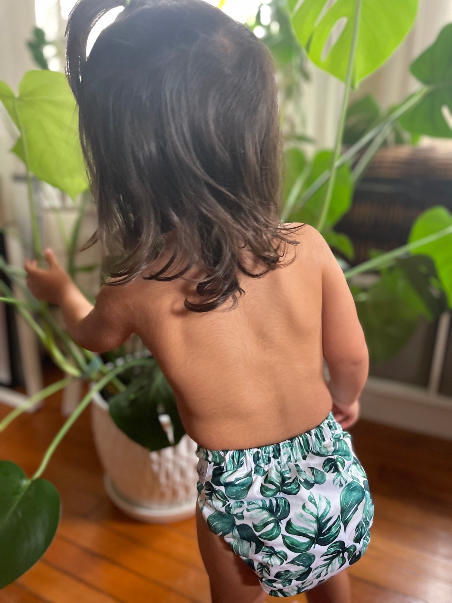 Child wearing a leaf-patterned diaper standing indoors with plants in the background