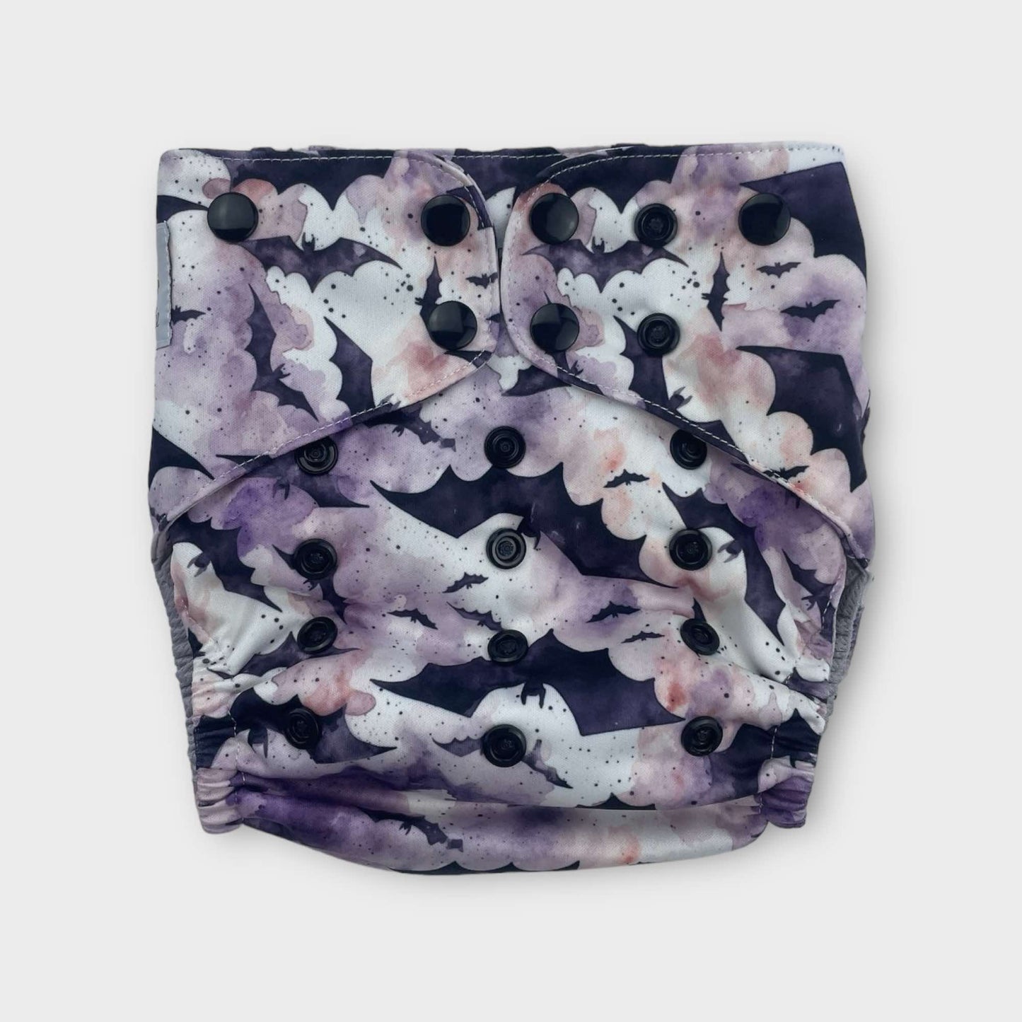 A pocket style wickham wild cloth diaper with a white, purple, and pink watercolor background and black silhouettes of bats of various sizes. The reusable diaper has black snaps.