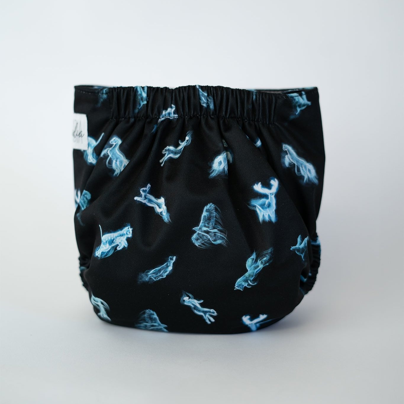 The back view of a pocket cloth diaper. The black fabric features glowing blue spirit animals in a wispy, ethereal style. The gathered elastic waistband is visible at the top. The luminous figures contrast sharply against the dark background.