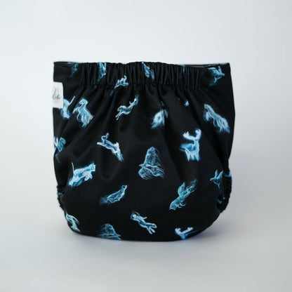 The back view of a pocket cloth diaper. The black fabric features glowing blue spirit animals in a wispy, ethereal style. The gathered elastic waistband is visible at the top. The luminous figures contrast sharply against the dark background.