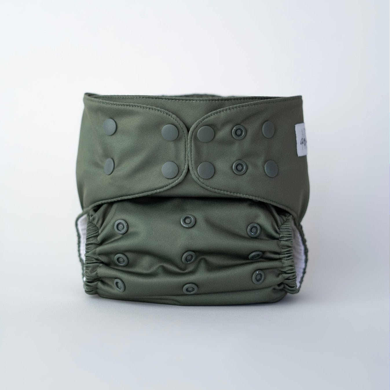 A reusable pocket cloth diaper in a muted, earthy moss green shade named Petrichor. This premium cloth diaper features multiple adjustable snaps for a customizable fit, ensuring comfort and leak protection for babies of all sizes. The soft, elastic leg openings and water resistant outer layer provide both flexibility and reliability. Front view.