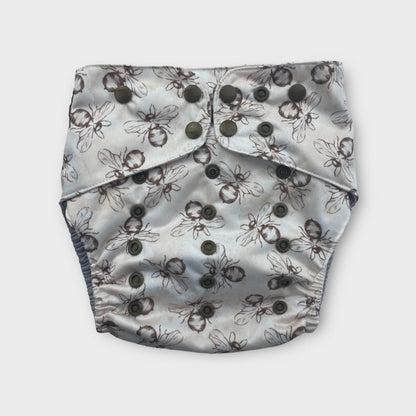 A wickham wild pocket style reusable diaper, With a light backgrouns and illustrations of bees in a brown tone.