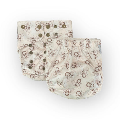  a photo of two pocket cloth diapers with a white background and illustrations of brown bumble bees. One diaper shows the front, the other shows the backj