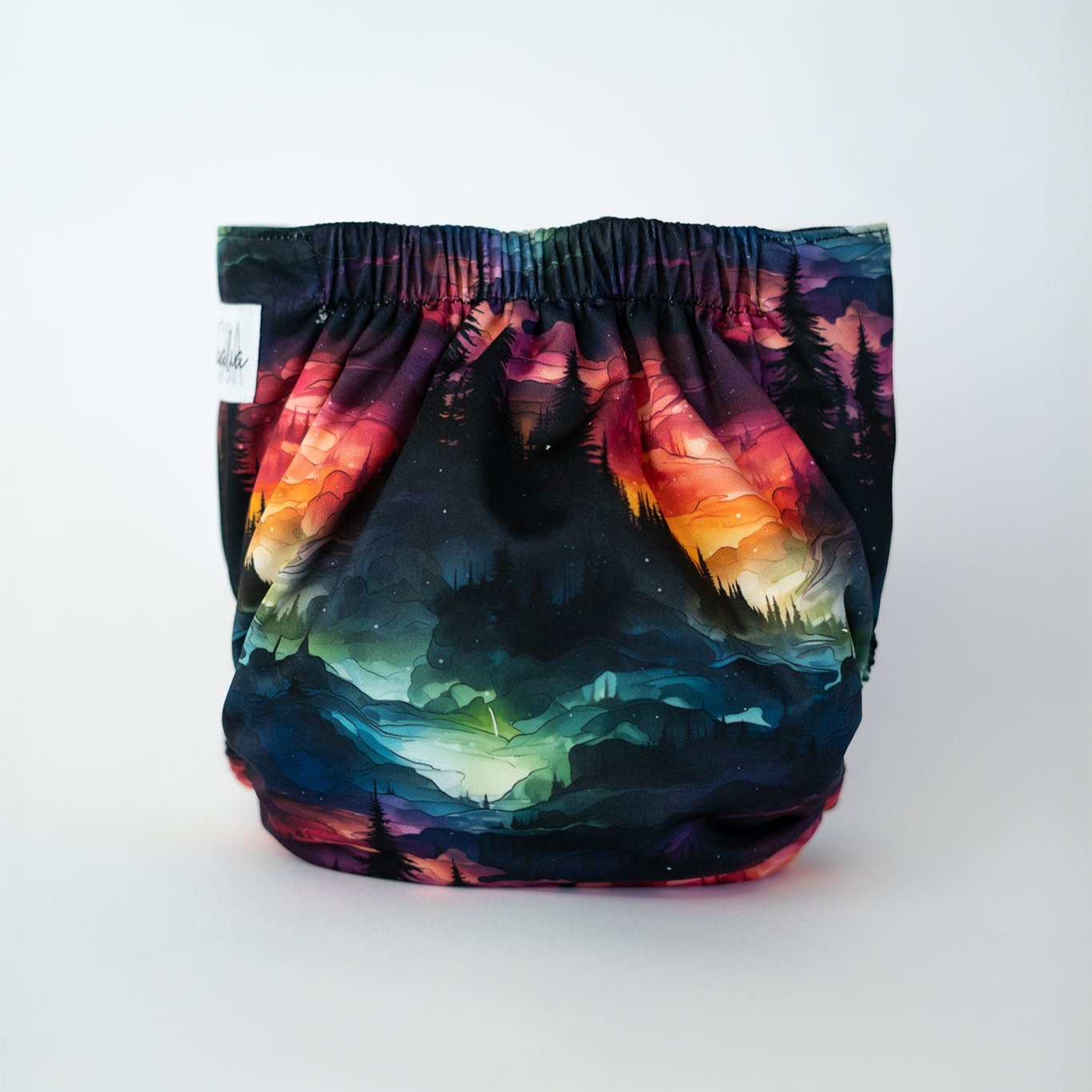 Vibrant cloth diaper showcasing a stunning landscape design. The rich blend of colors, from deep purples and blues to fiery reds and oranges, creates a mesmerizing aurora effect over a forested mountain scene. This reusable diaper offers both artistic flair and comfort for your baby. Rear view.