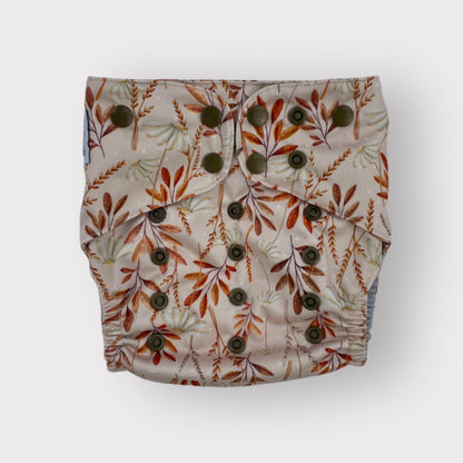 Floral patterned Wickham Wild Pocket style cloth diaper with buttons on a white/cream background. The foliage is in warm reddish-orange hues.