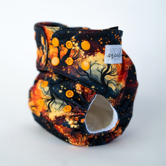 A pocket style cloth diaper from Arcadia’s Nursery shown at a slight front angle in the Autumn print. The fabric displays rich oranges, swirly black, and leaf shapes for an autumnal look. Coordinating orange snap closures along the waist and rise provide an adjustable fit, and the curved leg openings highlight the sculpted, performance focused design.
