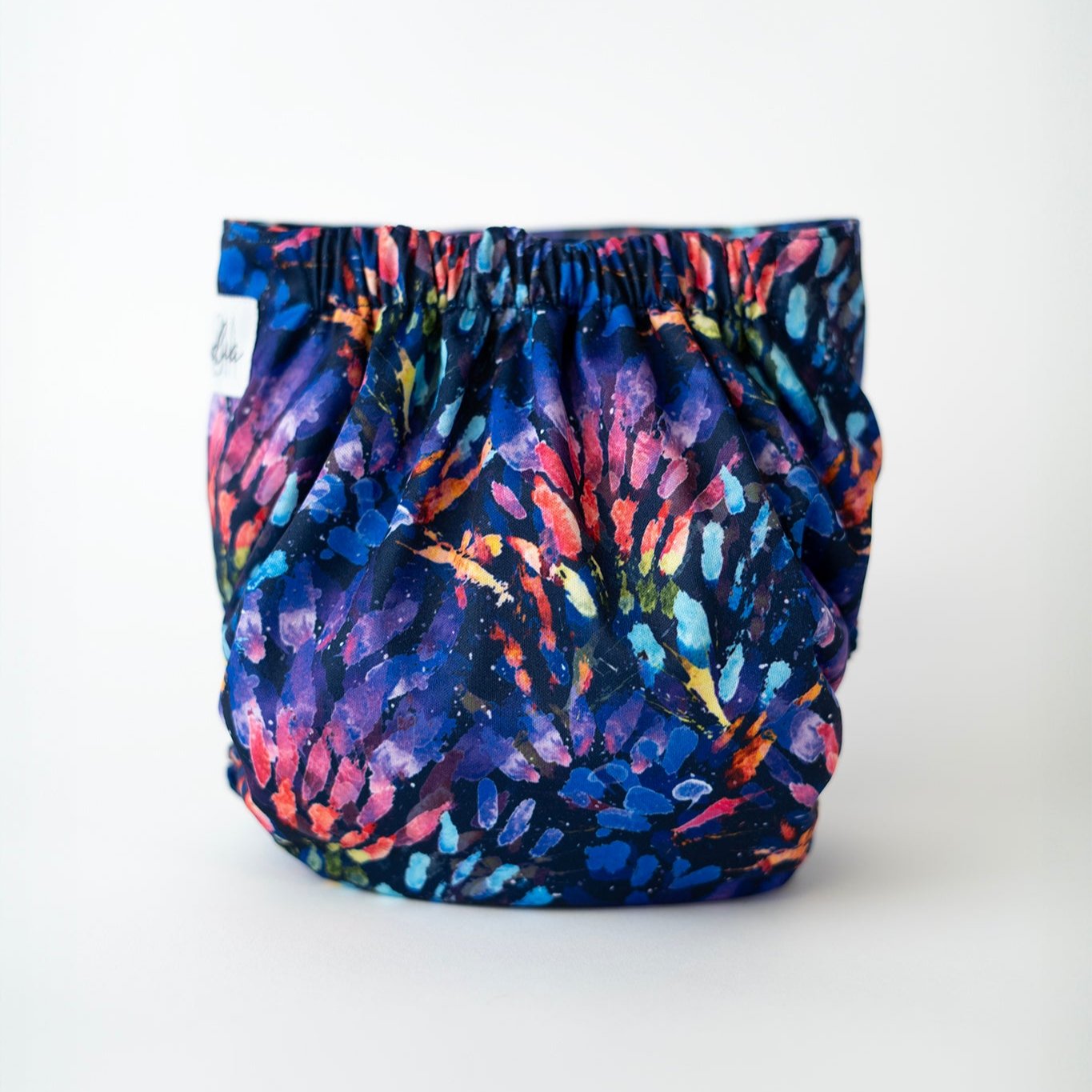 The back of an Arcadia’s Nursery pocket style cloth diaper displayed flat against a white background. The bold, abstract print continues across the full seat with rich jewel tones and layered brushstroke textures. Gathered elastic at the waist and legs highlights the contoured fit designed for comfort and leak protection, while the smooth outer shell showcases the full pattern uninterrupted.