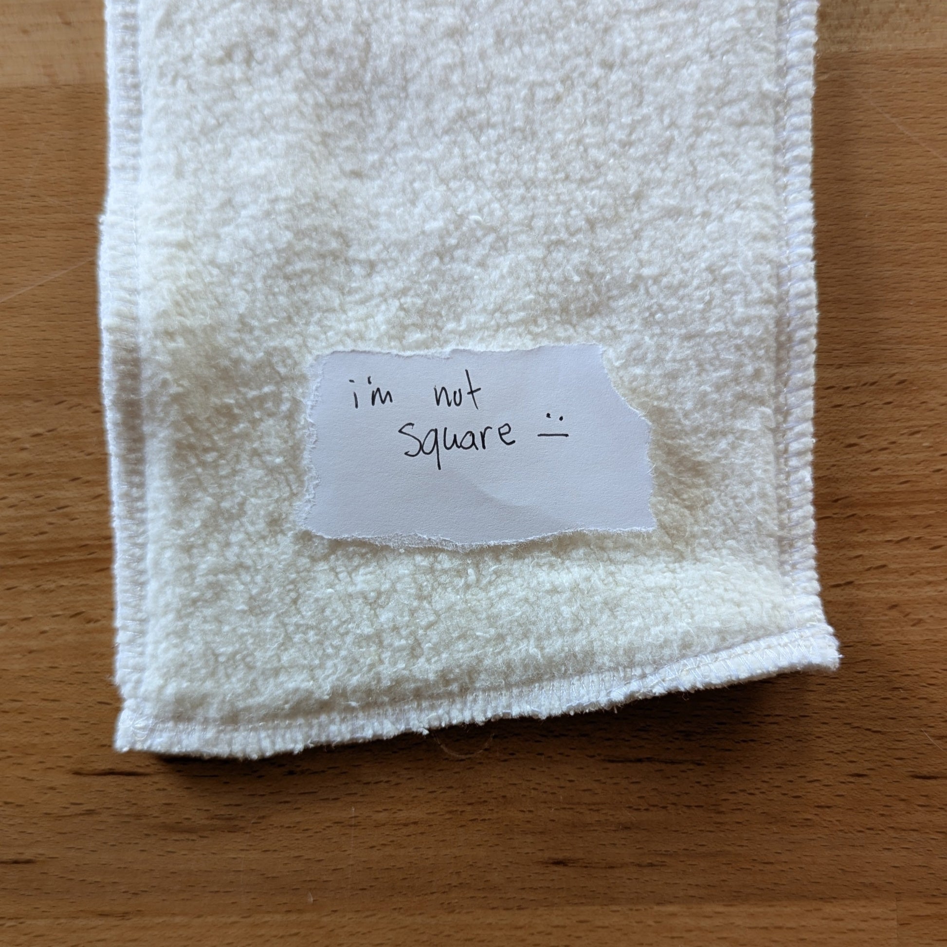 a photo of a seconds quality hemp cotton insert with a torn paper note on top that reads "I'm not swuare :|"