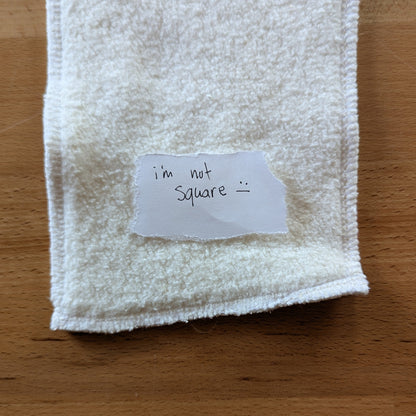 a photo of a seconds quality hemp cotton insert with a torn paper note on top that reads "I'm not swuare :|"