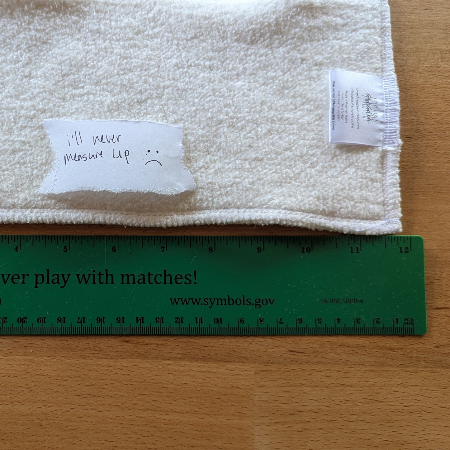 A cloth diaper insert next to a ruler with a paper that reads "I'll never measure up" and a frown face on the paper