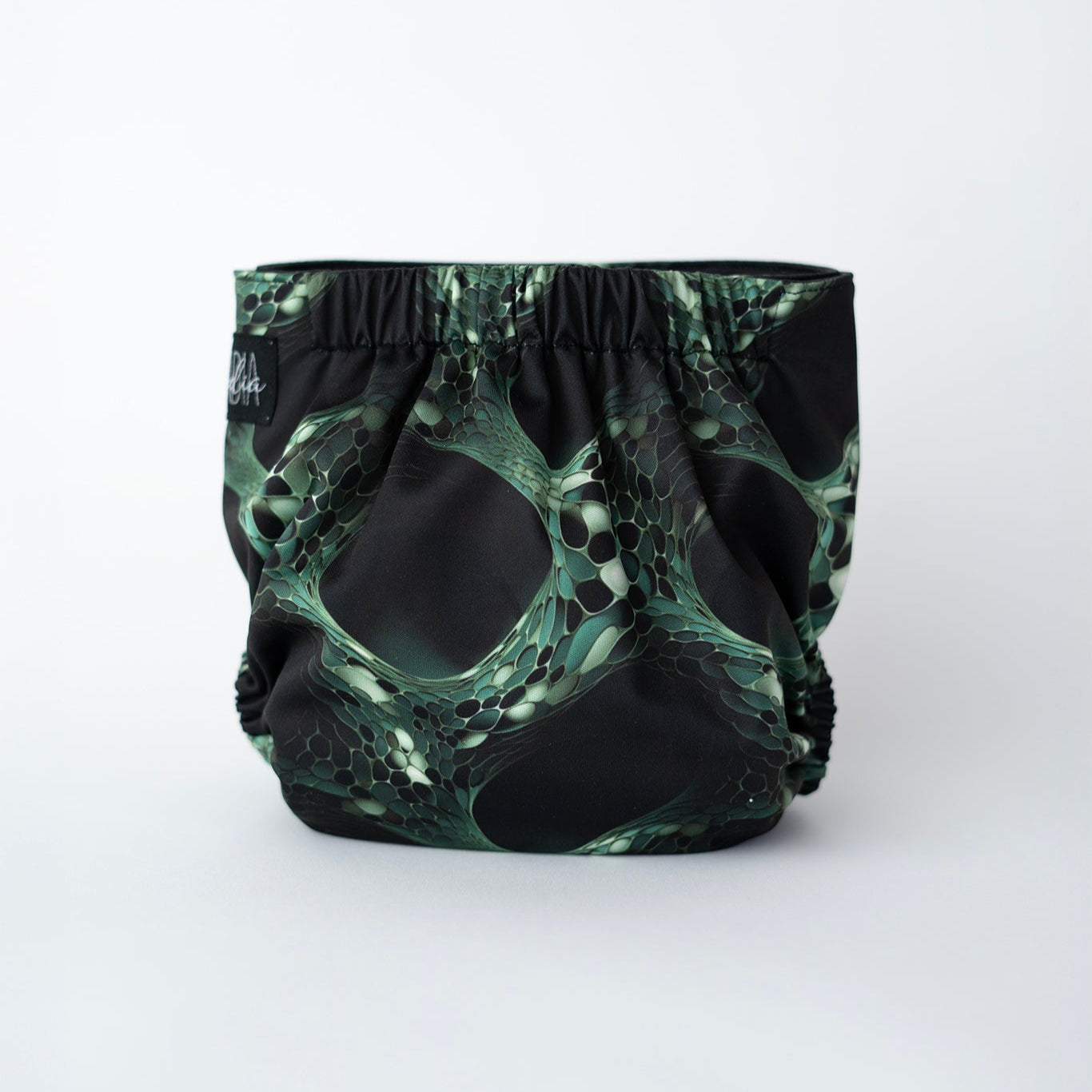 Reptile inspired pocket cloth diaper featuring a sleek green and black scale like pattern, resembling interconnected cells on a black background. This reusable diaper features a black logo tag and secure comfortable elastics. Rear view.